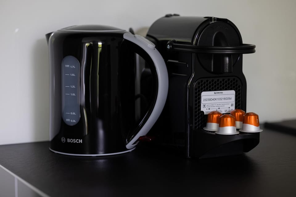 A close-up of coffee and tea accessories, including a modern coffee pod machine and stacked cups.