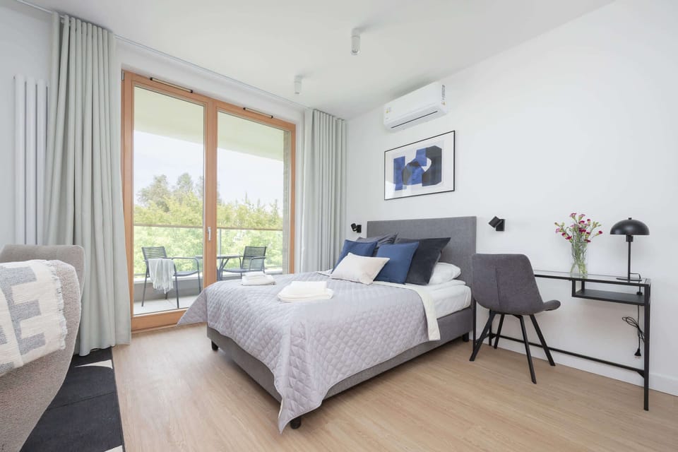 A bedroom with a soft green throw blanket and a large window letting in ample daylight.