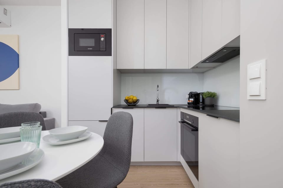A contemporary kitchenette with built-in cabinets, a compact layout, and dining chairs arranged around a table.