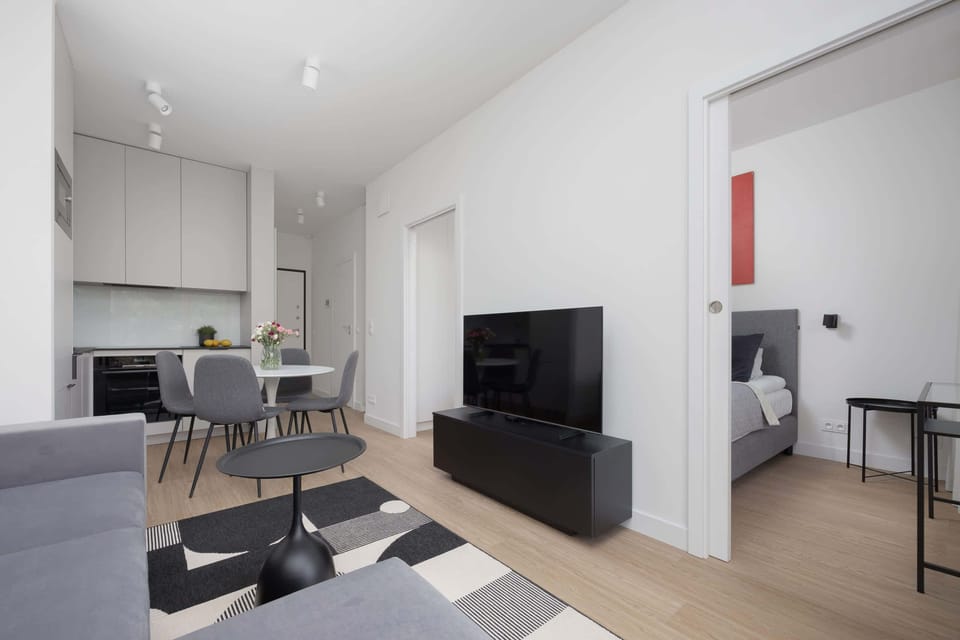 A compact lounge area with a wall-mounted TV, gray furniture, and a black and white rug.