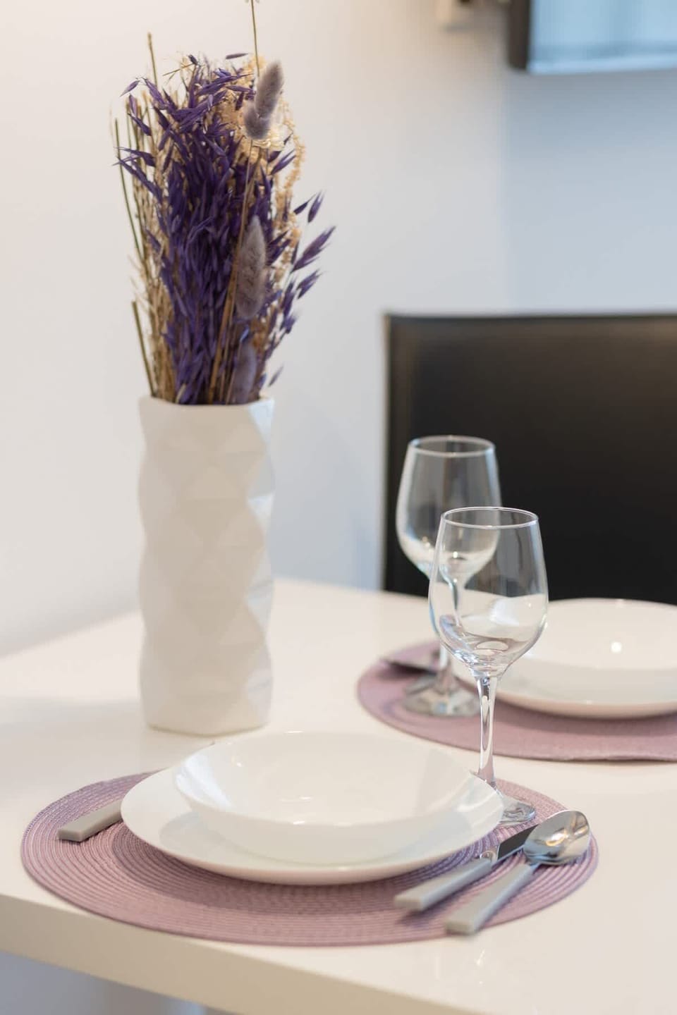 A close-up of a dining setup with a lavender vase, white plate, and an elegant touch.

