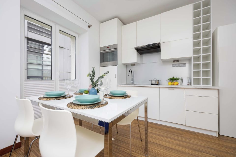 A dining area with a round white table and four chairs. The space is connected to a modern kitchen with white cabinets.