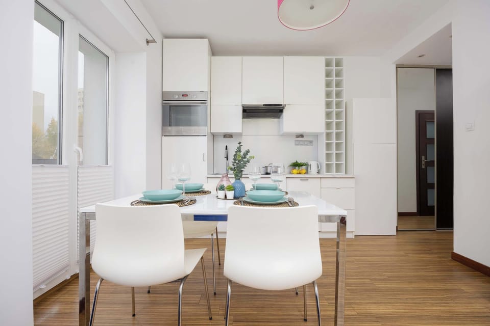 The kitchen has sleek white cabinets, a small countertop, and basic appliances like a kettle and microwave. It’s compact and functional.