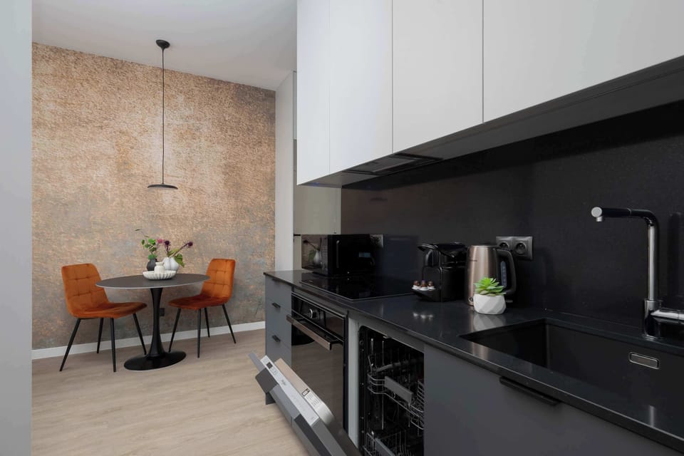A modern kitchen with sleek black cabinets and built-in appliances. In the background, a round dining table with stylish chairs creates a cozy dining space.