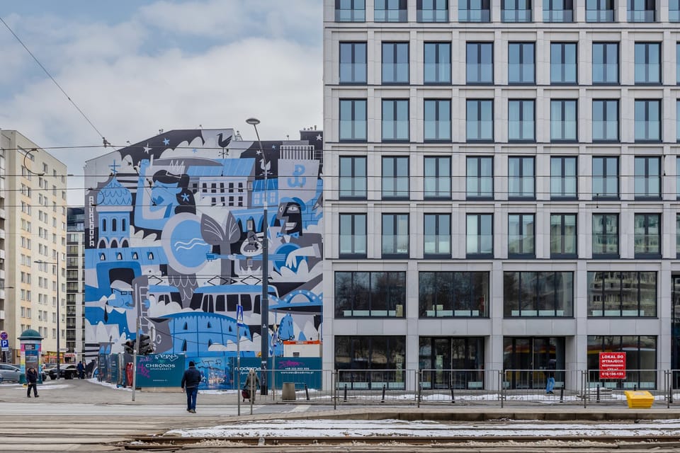 A view of the exterior of a contemporary building with large glass windows. A colorful mural decorates the side of the structure.