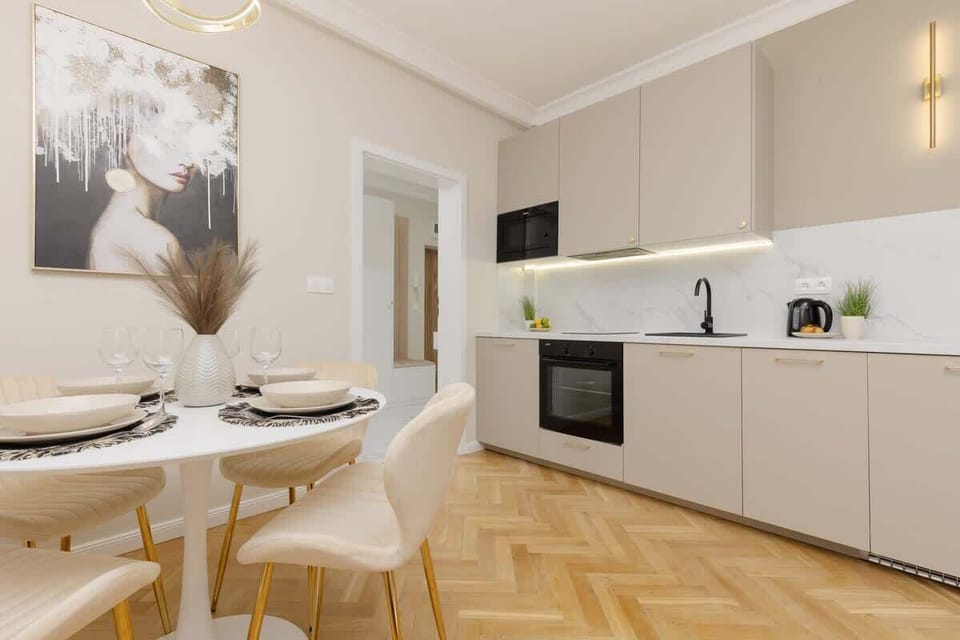 A bright open-plan kitchen with a dining area, featuring modern cabinetry, built-in appliances, and a round table with chairs.
