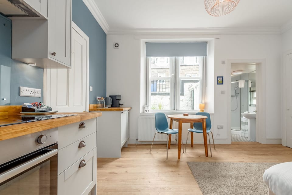 Contemporary kitchen with wooden countertops and white cabinets, adjacent to a round dining table near a window offering plenty of daylight.