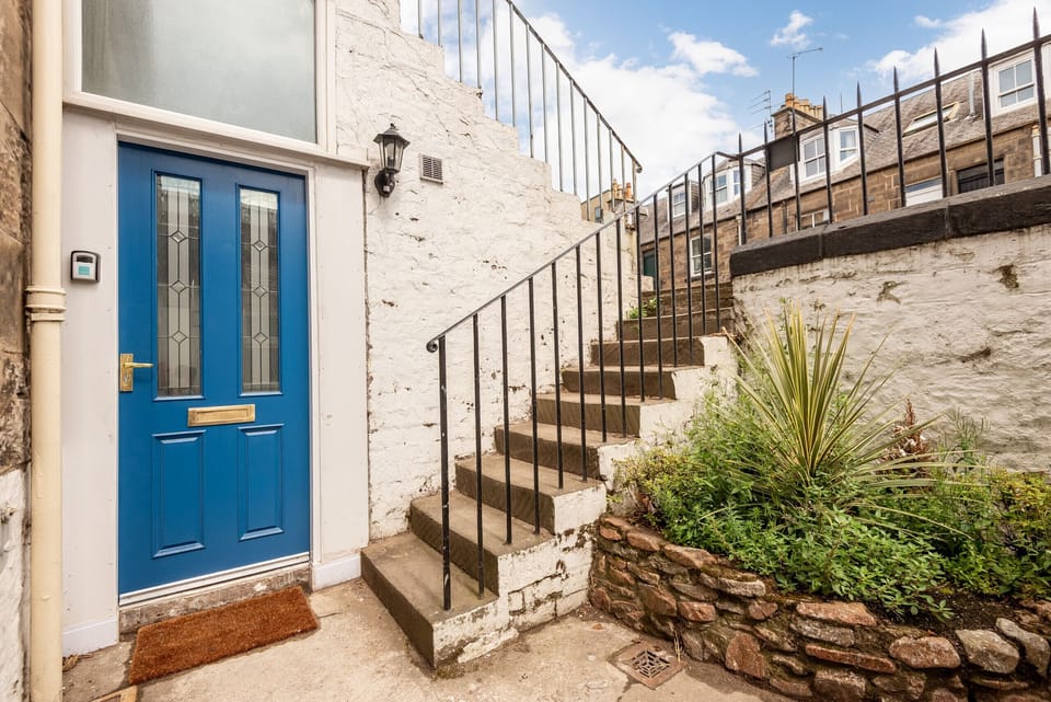 Blue door at base of stairs next to stone wall and planted border.