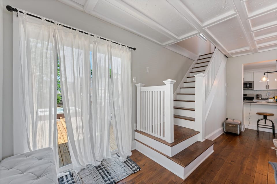 Step into comfort and style! This inviting space features beautiful hardwood floors, a modern staircase, and large glass door with sheer curtains that open to a private deck and hot tub. 