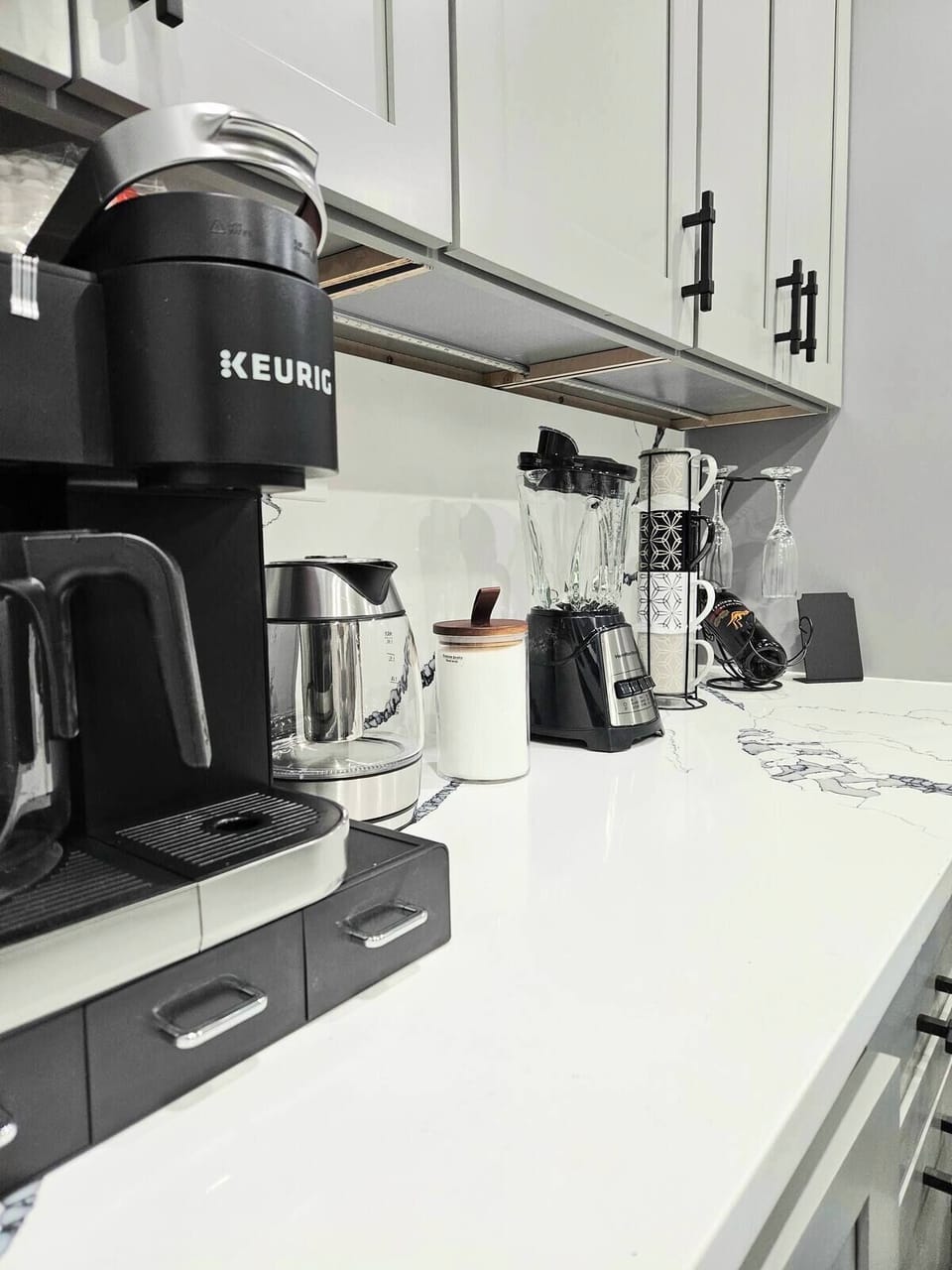 Beverage corner with a coffee machine, blender, and mugs.