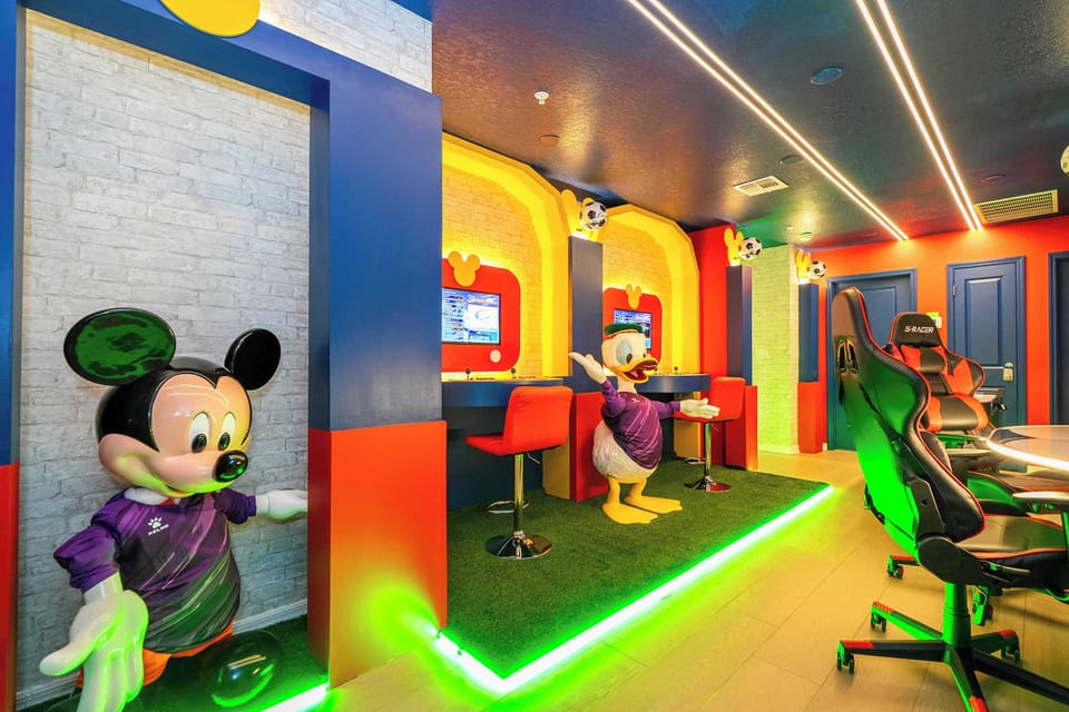 Dive into fun in this vibrant game room with playful Mickey and Donald décor, neon accents, and cozy gaming chairs-perfect for all ages to enjoy a whimsical retreat!