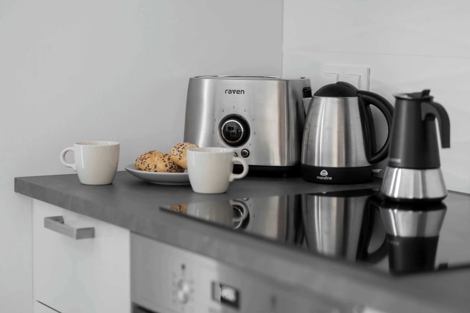 A clean and minimal kitchen space equipped with appliances like a microwave, a kettle, and a coffee machine, all neatly arranged on a black counter.