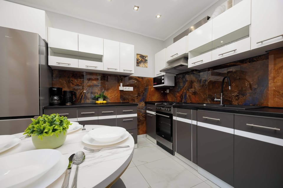 A kitchen and dining area with black and white cabinetry, orange accents, and marble-style flooring.