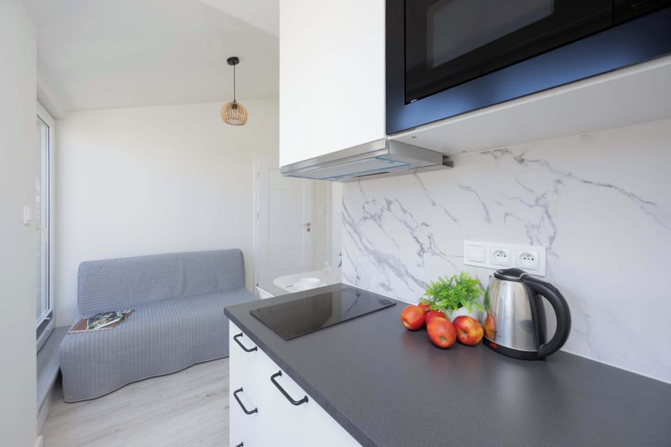 A close-up of a kitchen counter featuring a kettle, red peppers, and a tomato next to the sink.