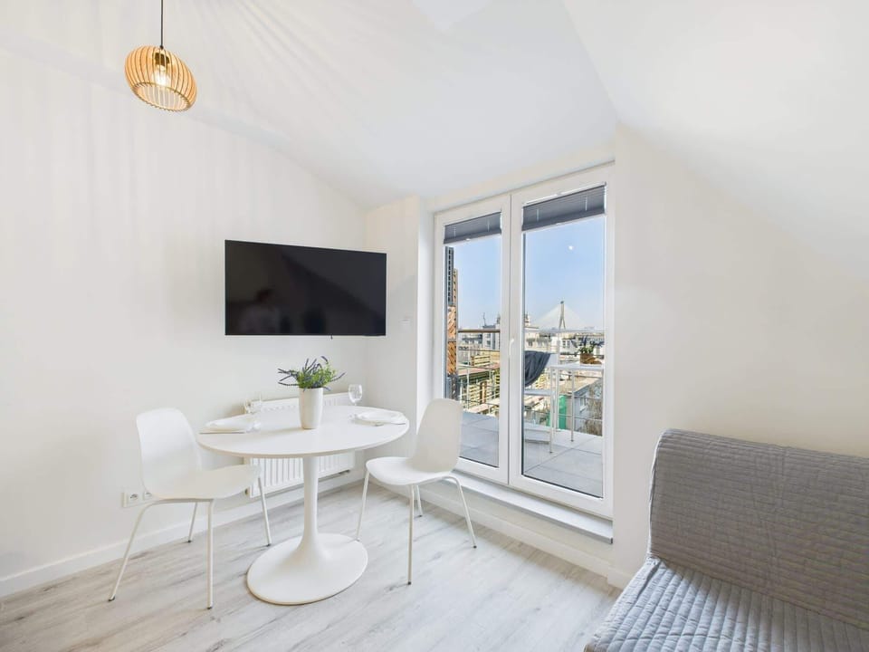 A bright corner with a round dining table, TV, and windows that bring in ample daylight. The white walls and light tones create an open feel.