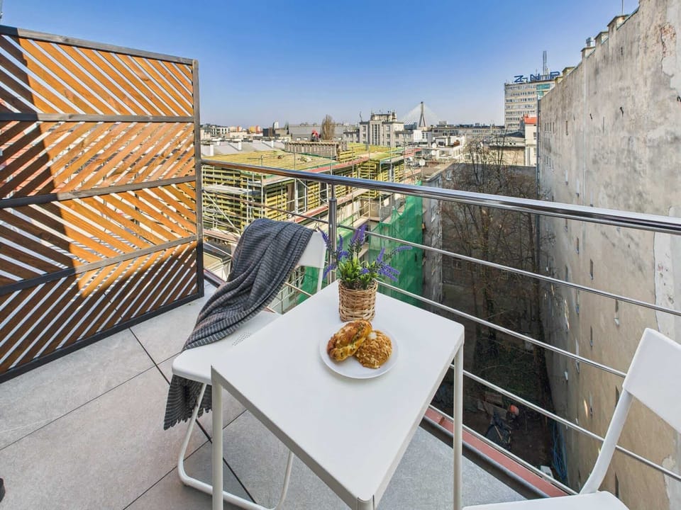 A charming outdoor balcony setup with a small table and two chairs, perfect for enjoying a coffee with a city view. Wooden fencing adds warmth and privacy.