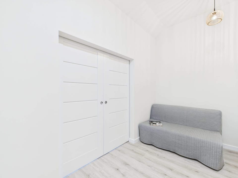 A living area featuring a gray sofa bed and a white cabinet. Sloped ceilings and wooden floors maintain a warm, open atmosphere.