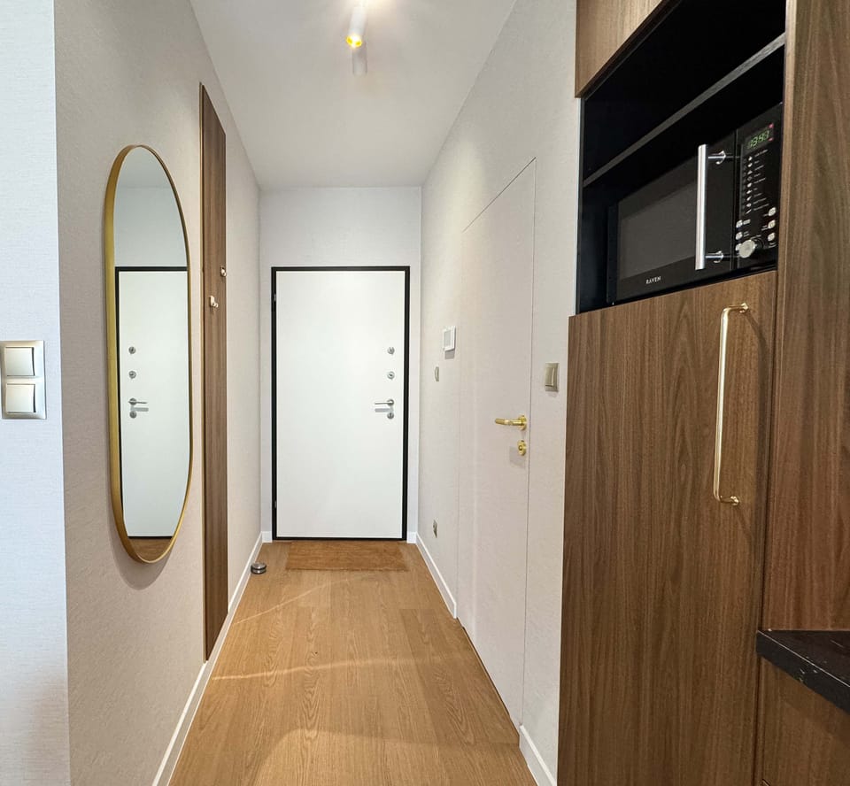 A long, bright corridor with wooden floors and white walls. Natural light fills the space, leading to rooms in the distance.