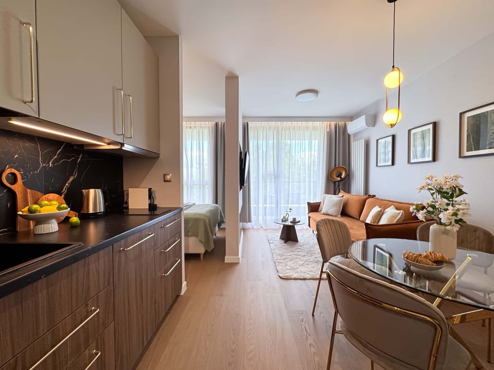 A modern kitchen with dark cabinets and a long counter, opening into a bright living area. The design blends functionality with contemporary style.