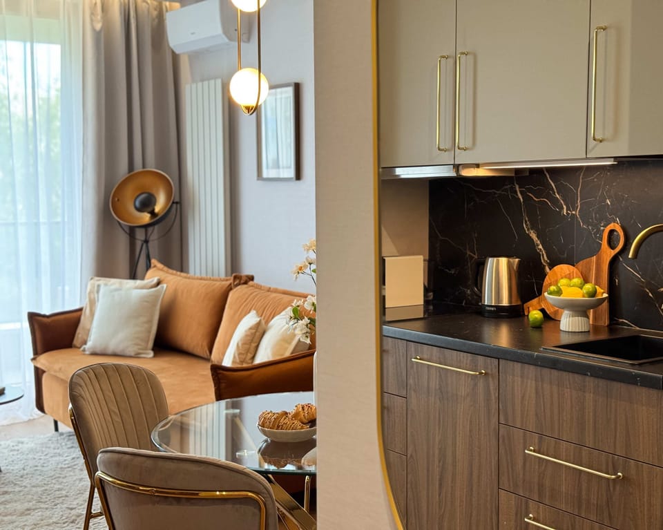 A stylish living area with a sofa, coffee table, and open kitchen. The space features wooden finishes and soft lighting for a homely ambiance.
