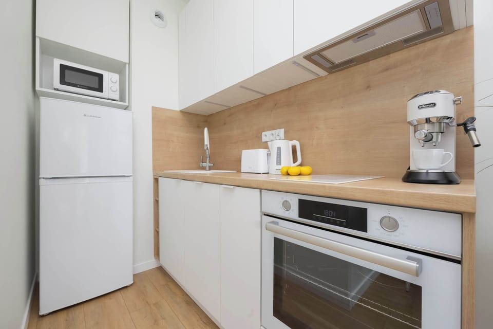 A modern kitchen equipped with an oven, microwave, and coffee machine. The space is bright, with wood and white finishes.