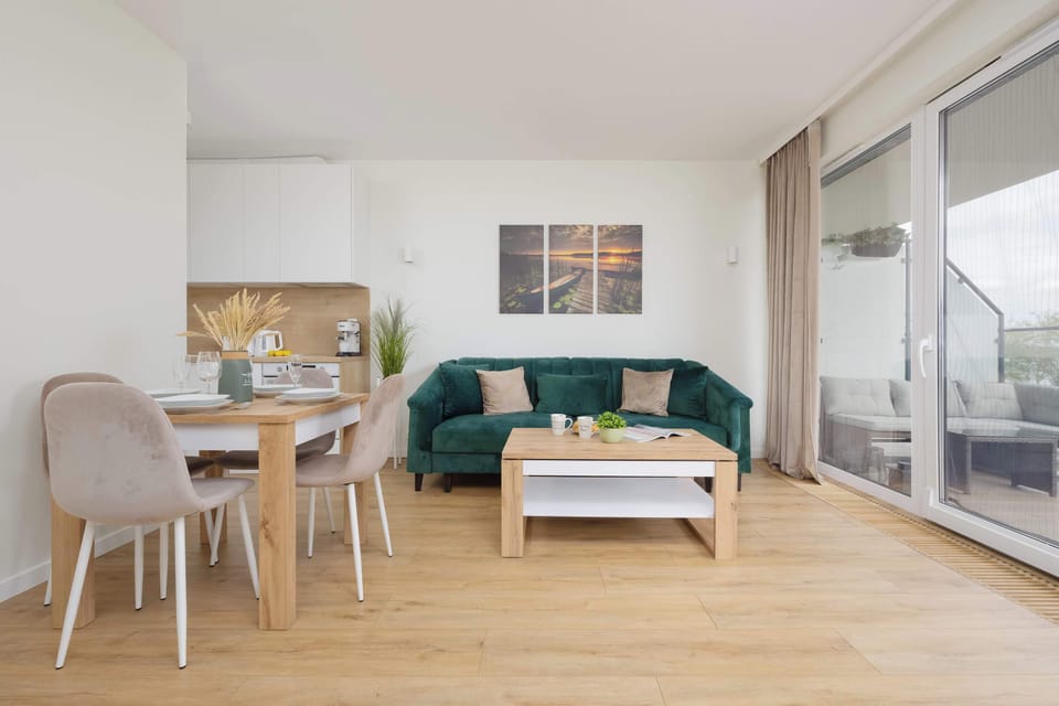 Another angle of the living room with a green sofa and large windows. Sunlight fills the space, creating a bright and welcoming ambiance.