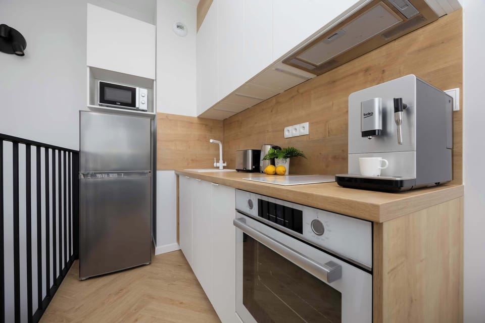 The kitchenette equipped with white furniture and stainless steel appliances looks modern and neat.