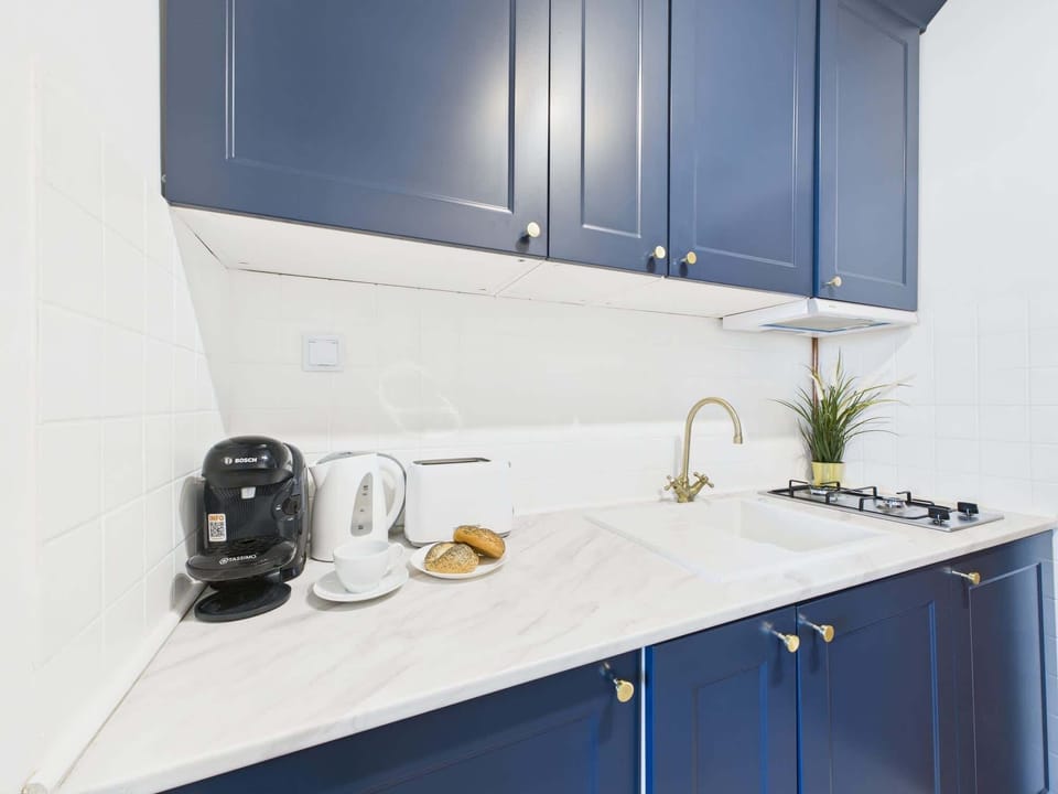 A functional kitchen corner with deep blue cabinetry, kettle, toaster, and modern countertop lighting.