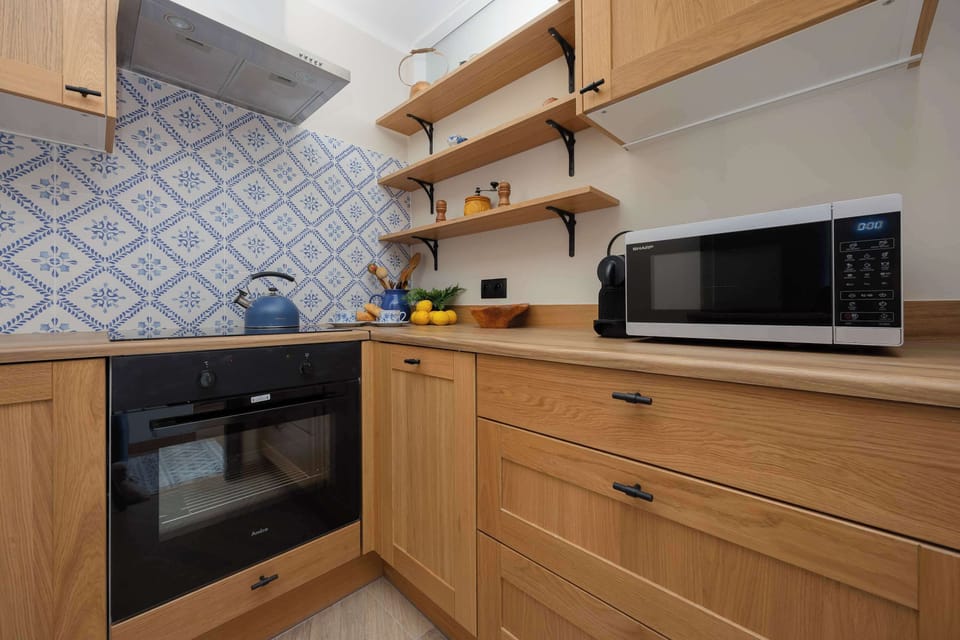 A compact kitchen with wooden cabinets, an oven, microwave, and a backsplash with blue and white tiles.