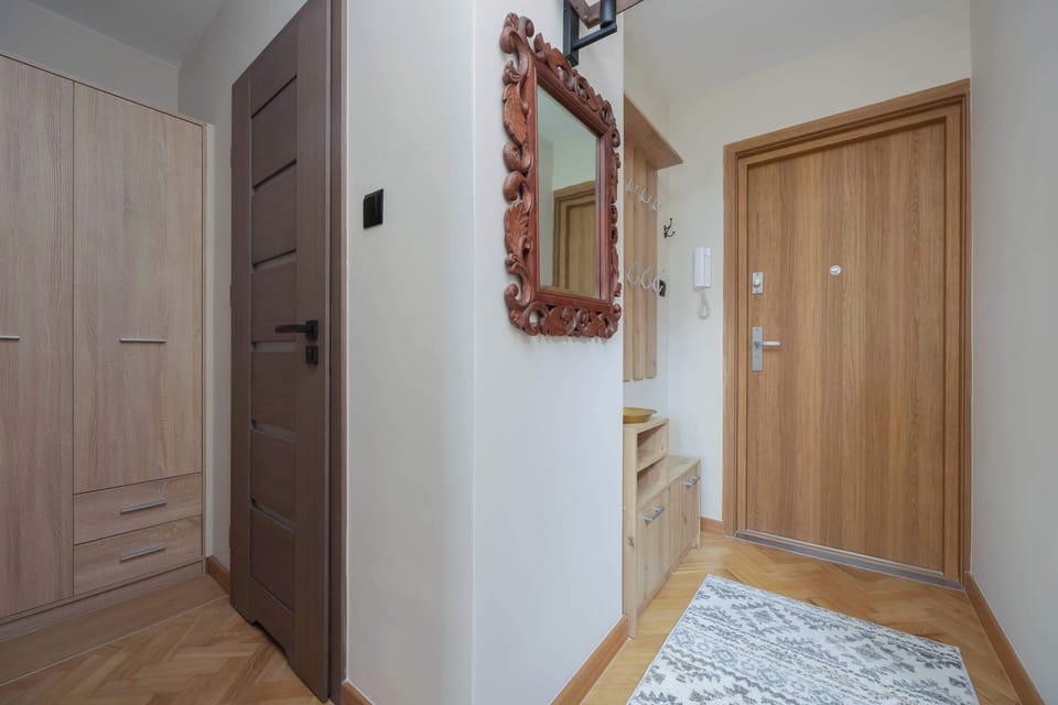 A hallway with a wooden door, a mirror, and light-colored flooring.