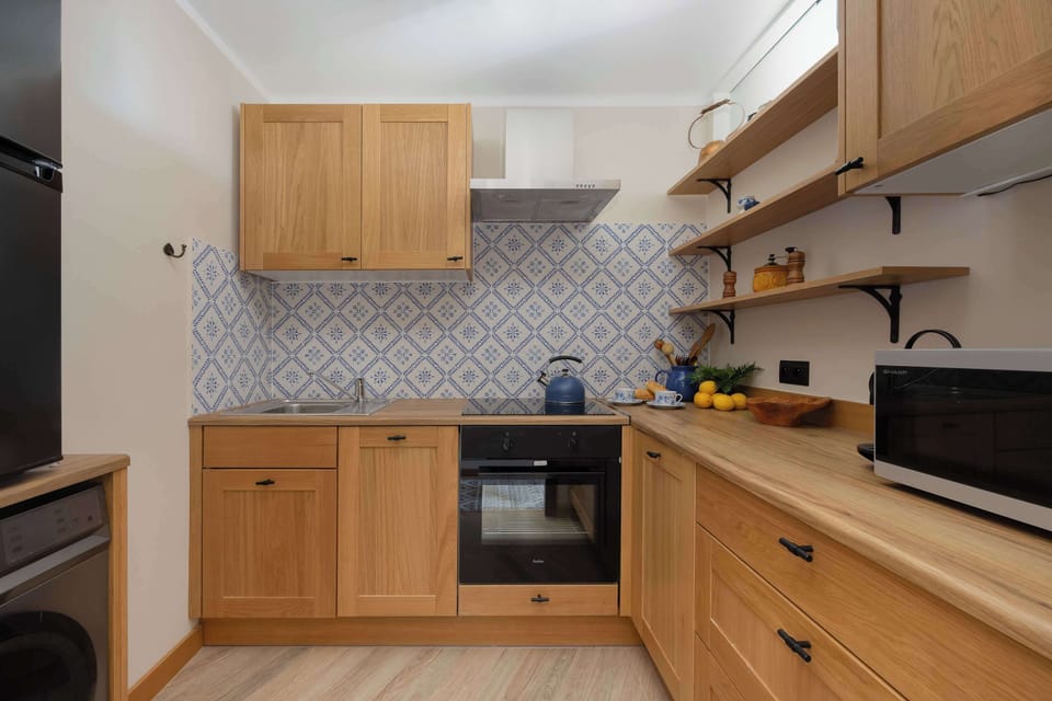 A small kitchen featuring open wooden shelves holding various utensils and decor items, alongside a countertop with a microwave.