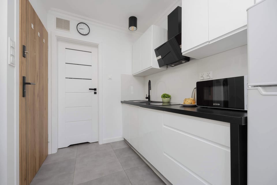 A compact kitchen area with black countertops, white cabinets, and a black electric kettle under sleek wall lighting.