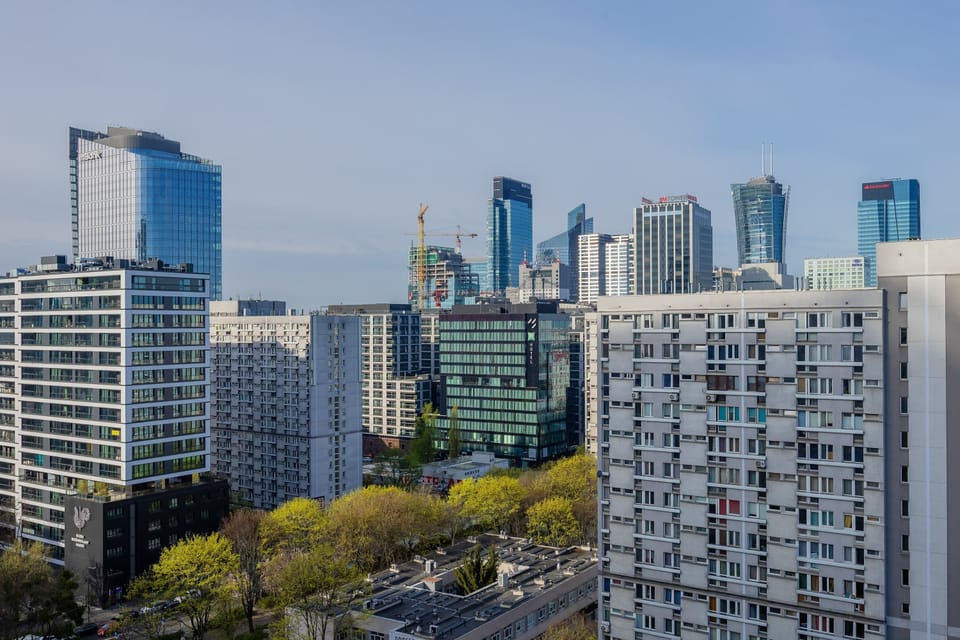 A wide cityscape view of Warsaw’s skyline with a mix of contemporary high-rises and greenery in the foreground.

