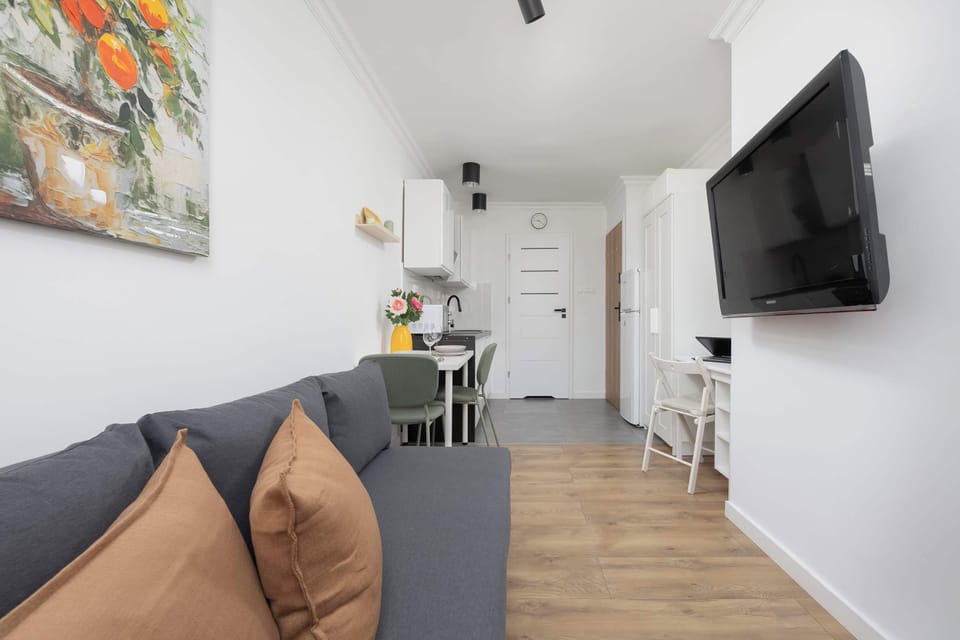 A double-seater gray sofa facing a mounted TV and window, styled with warm-toned pillows.

