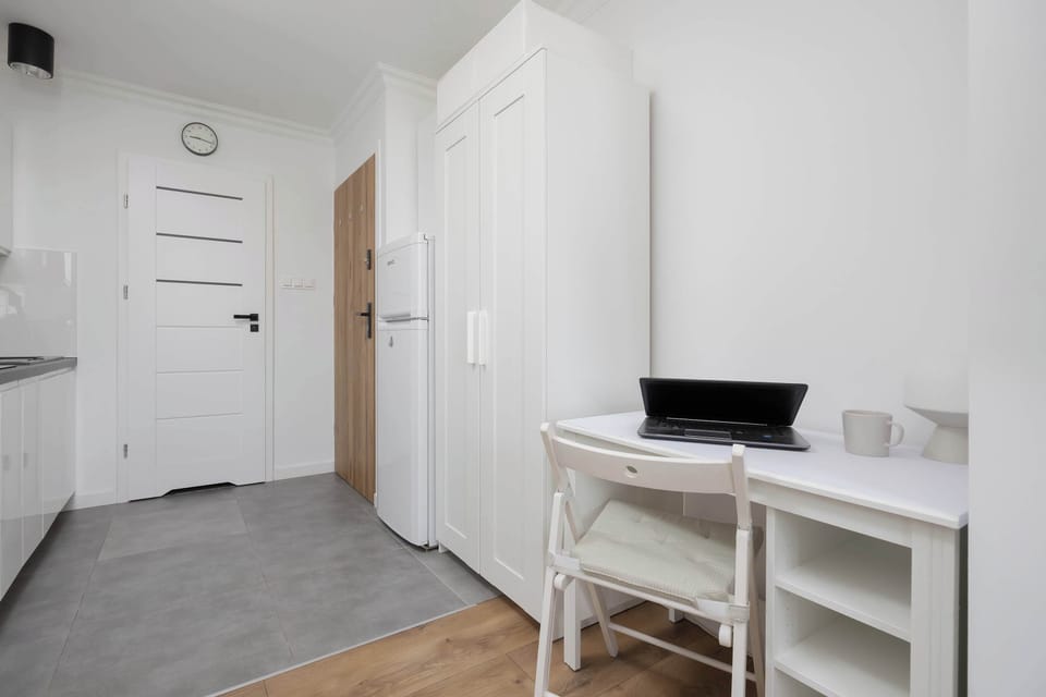 A small, neat workspace with a desk, chair, and desk lamp near the apartment entrance.

