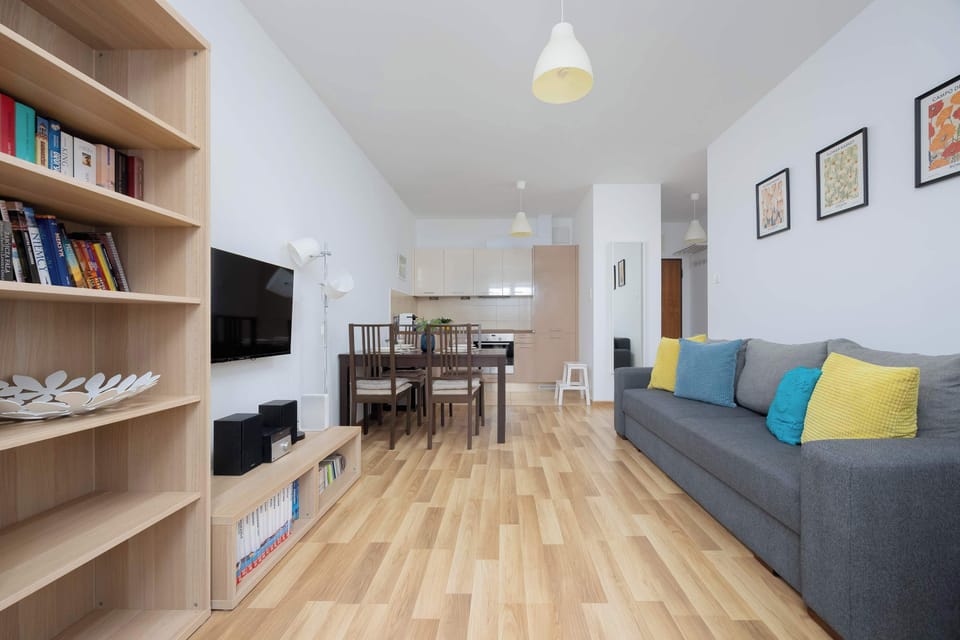 A long view of the living room showing the seating area on one end and the dining area on the other. The open layout feels spacious and bright with wooden flooring throughout.