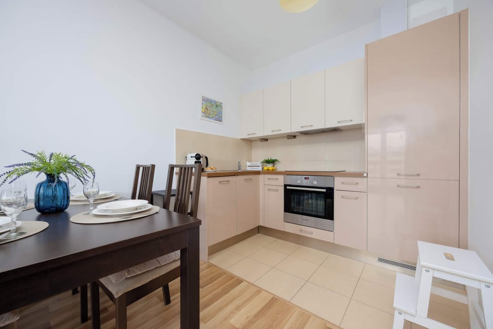 A modern kitchen with sleek white and beige cabinetry, a dining area visible in the corner, and decorative plants adding a touch of vibrancy.