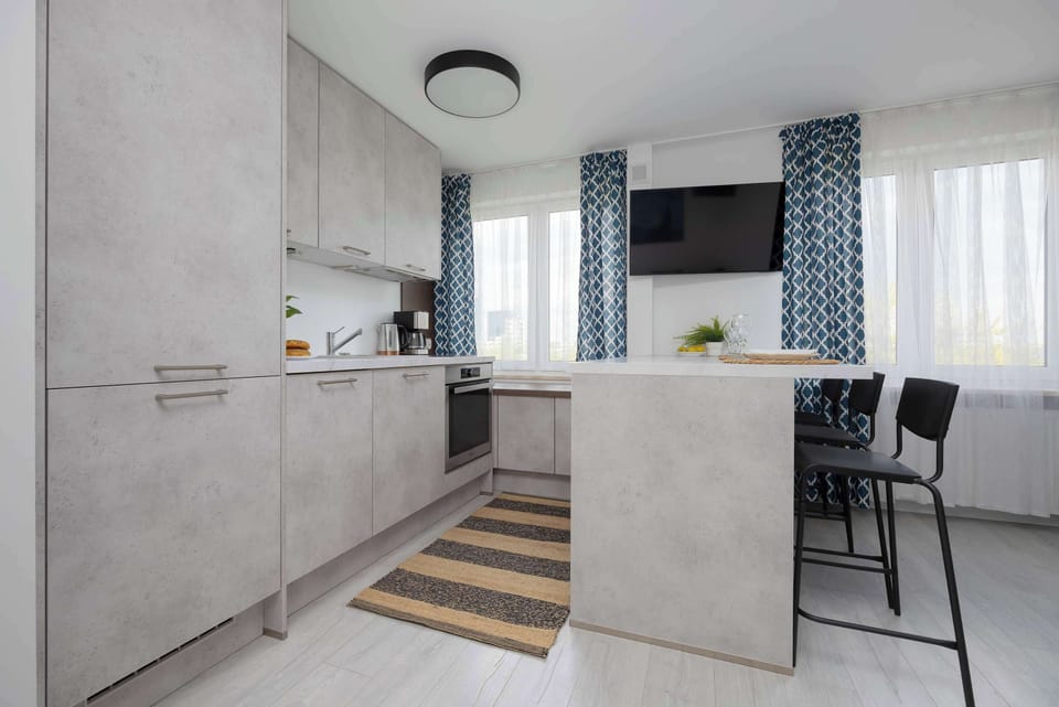 A kitchen and dining area with gray tones, a patterned curtain, and a table set for four with a view of the hallway.