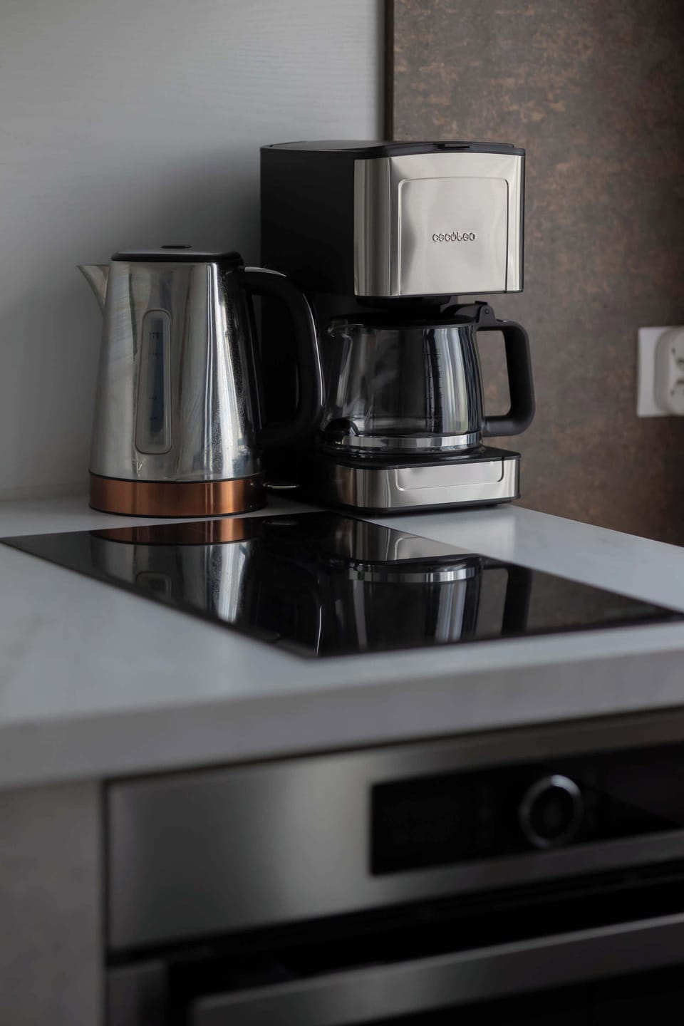 A close-up of a coffee-making station featuring a coffee machine and electric kettle placed on a white countertop.