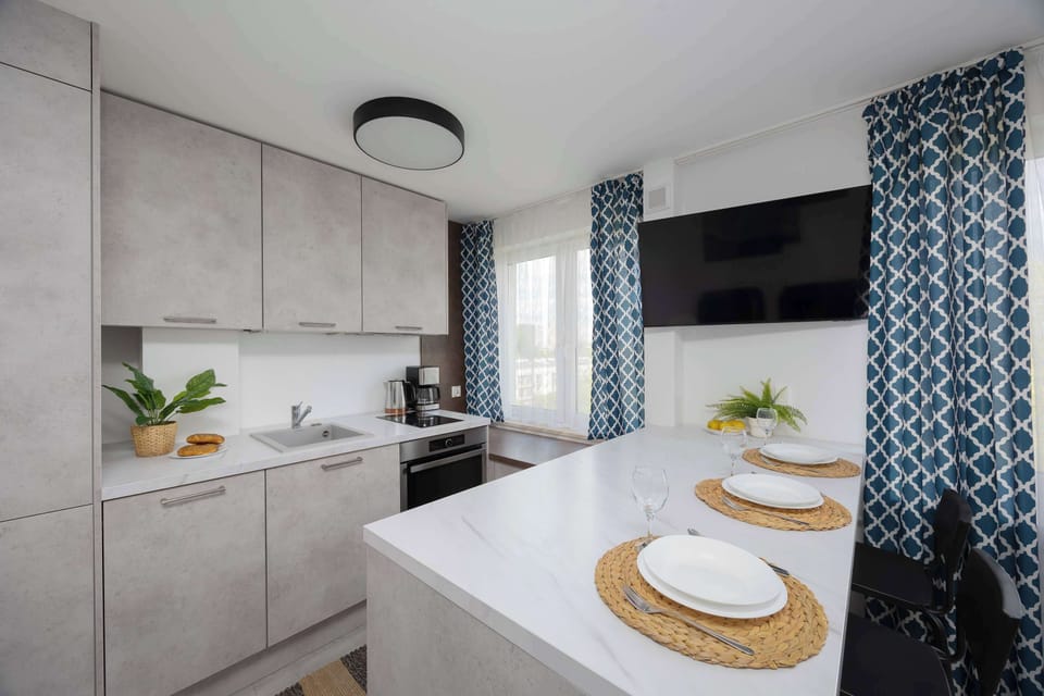 A well-lit kitchen with a marble-style backsplash, white cabinetry, and a window framed with patterned curtains.