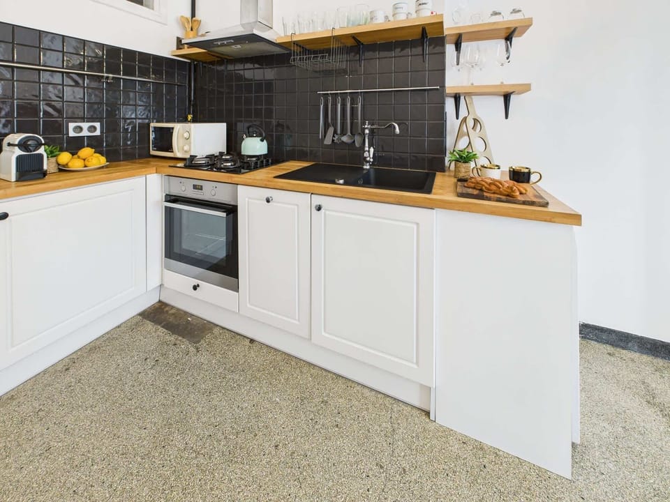 Modern kitchen space featuring black tile backsplash, open wooden shelves, and essential appliances.