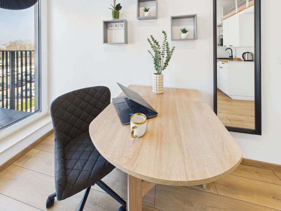 A view of the dining table near the window with a decorative plant and a comfortable chair. The simple yet elegant setup is ideal for meals or work.