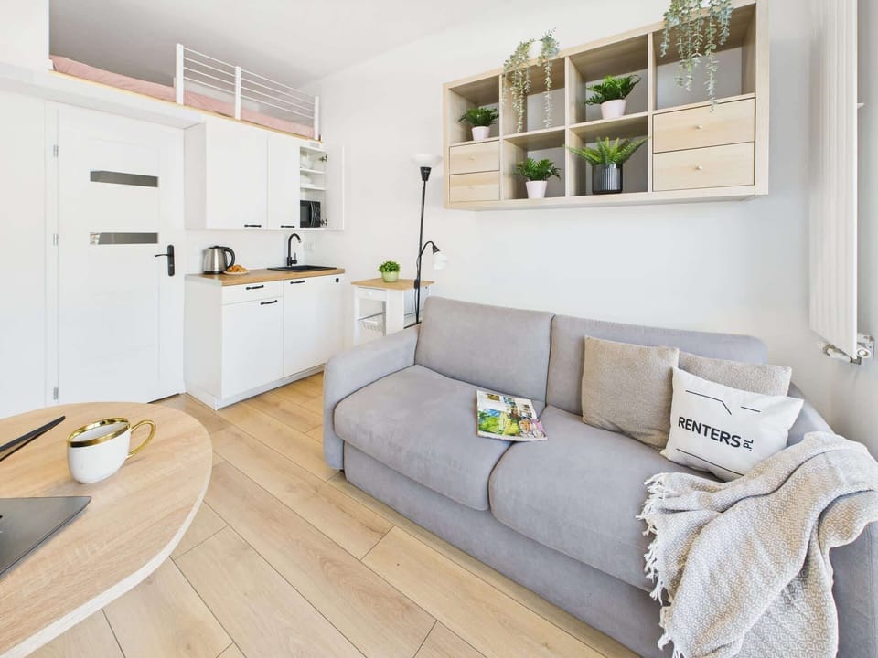 The open-concept living area combining the sofa, kitchen, and dining space. The white walls and wooden flooring enhance the modern aesthetic.