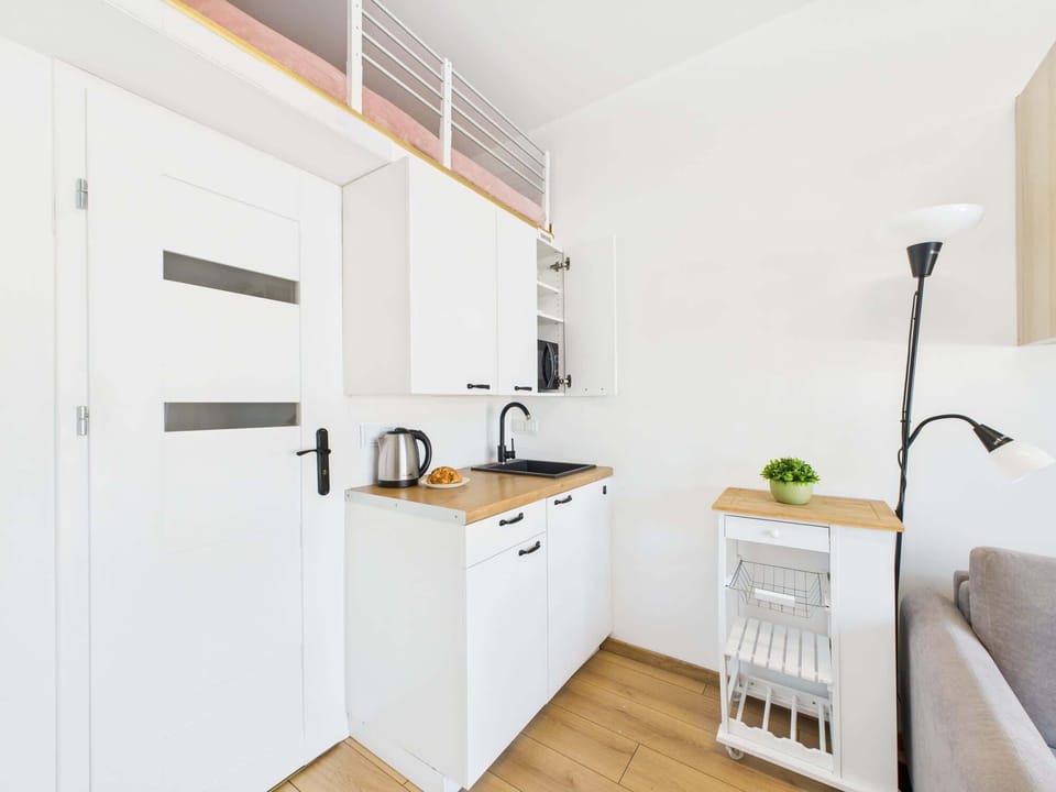 A modern kitchenette with white cabinets, wooden countertops, and open shelving. The compact design maximizes functionality and style.