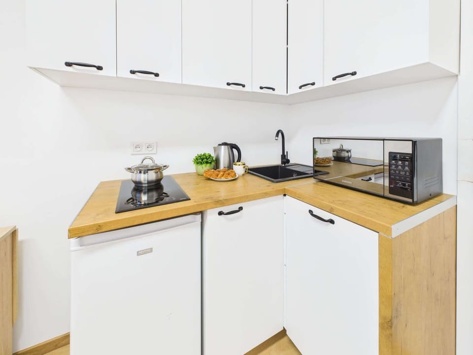 A modern white kitchen is equipped with built-in appliances. It features a microwave, a stove, and wooden cabinets for storage.