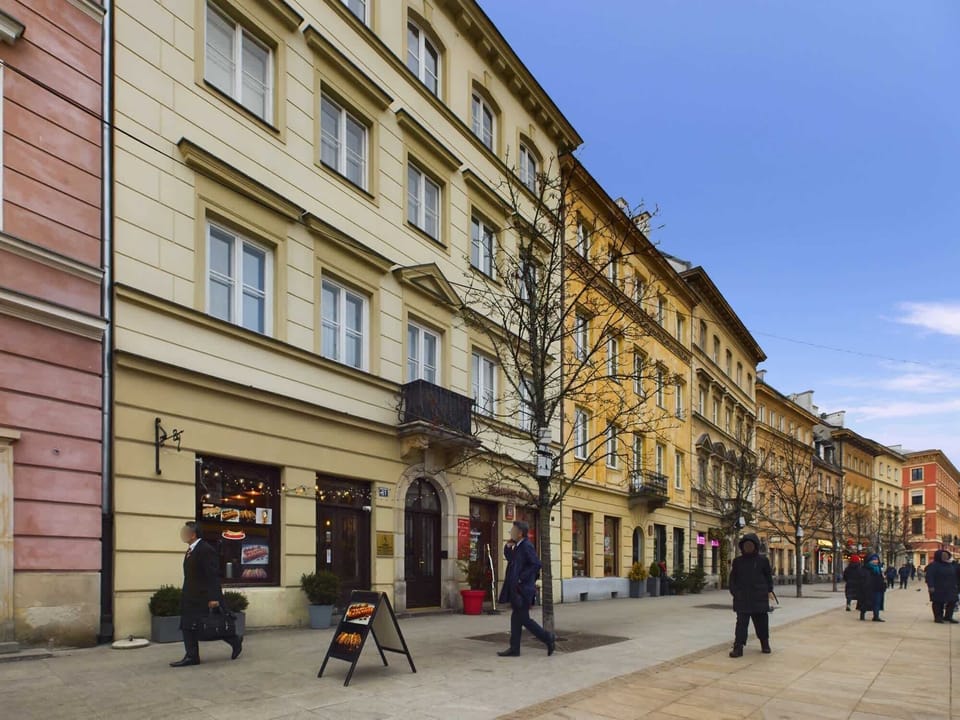 Another view of the cobblestone street, showing classic European buildings and a few pedestrians walking along the sidewalk.