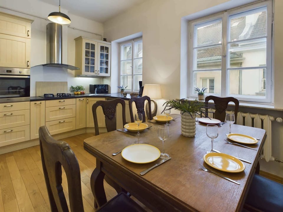 A spacious dining area with a wooden table and chairs, positioned near a window. The room is illuminated by natural light, enhancing the warm ambiance.