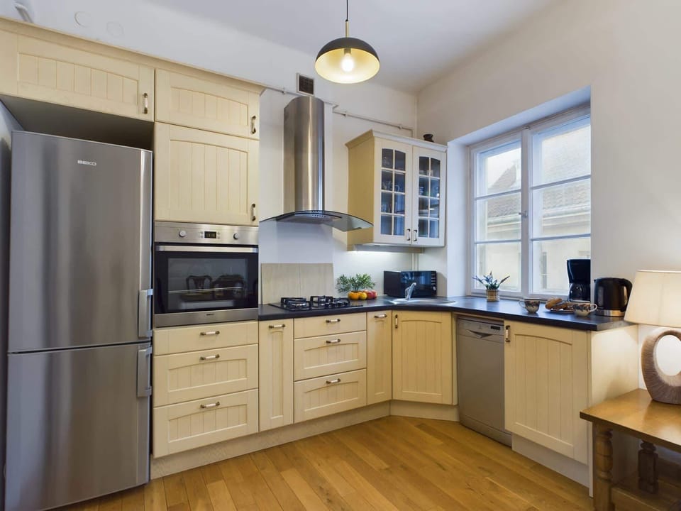 A kitchen with wooden cabinetry, white countertops, and modern appliances, including an oven and refrigerator. A small dining table is also visible.