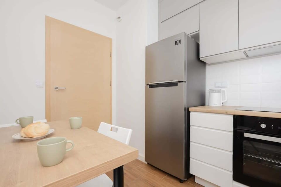 A kitchen with modern appliances, including a fridge, oven, and microwave. A dining setup is visible in the background.