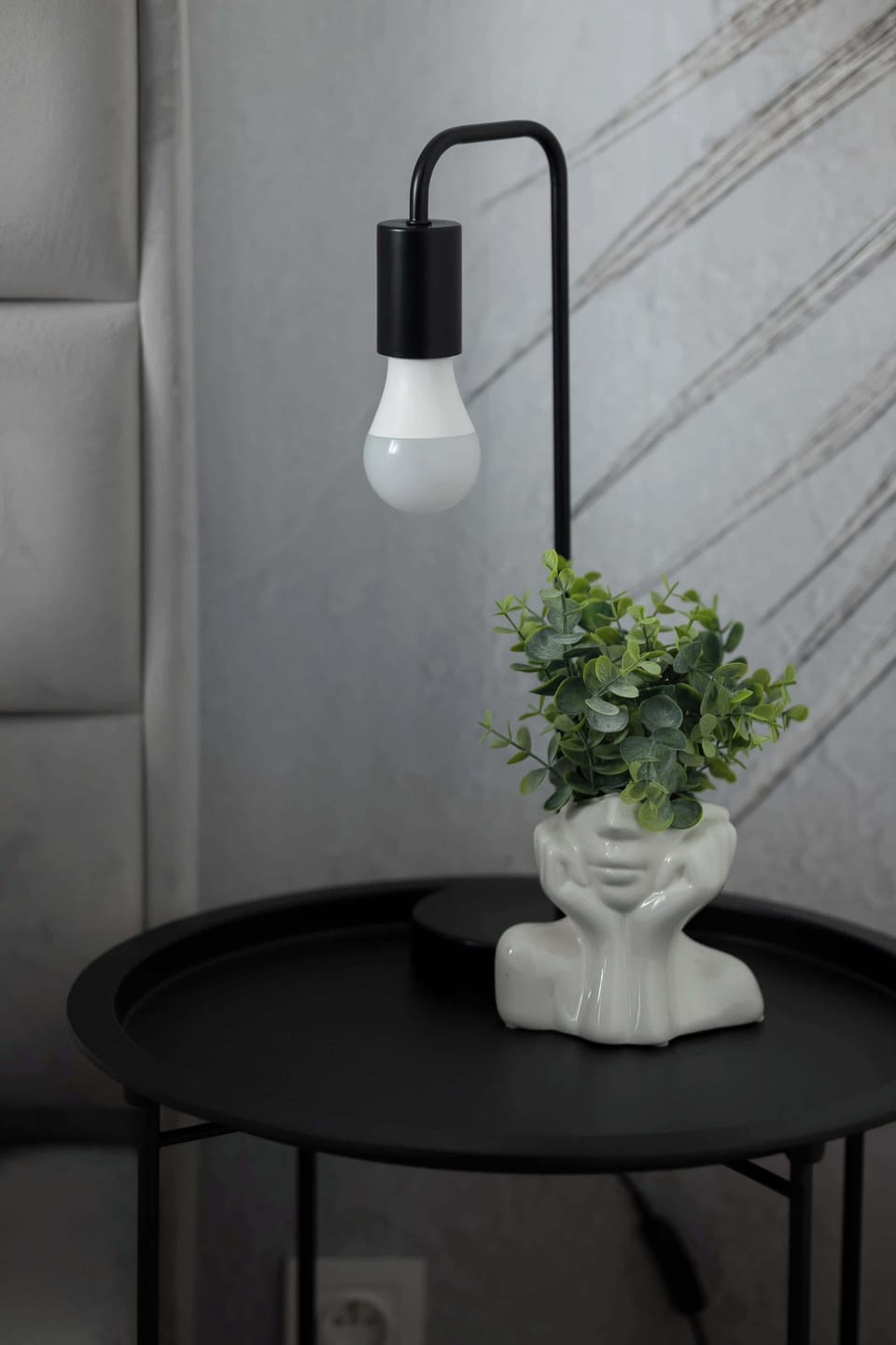 A small round table with a minimalist lamp and a vase of flowers, offering a cozy touch.